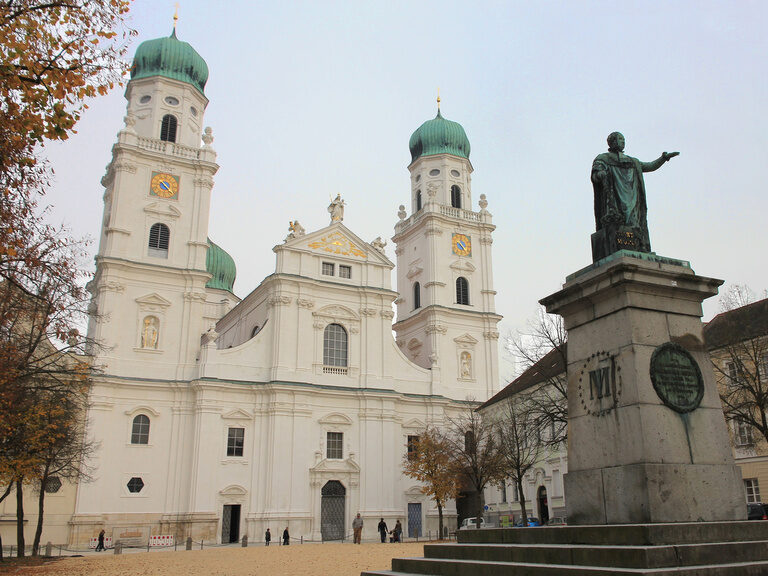Eine Bronzeskulptur steht auf dem Domplatz vor dem kirchlichen Wahrzeichen, dem Stephansdom in Passau.